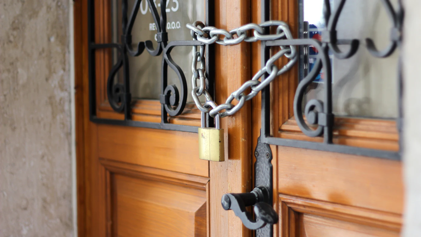 Wooden double doors held shut with a metal chain and brass padlock